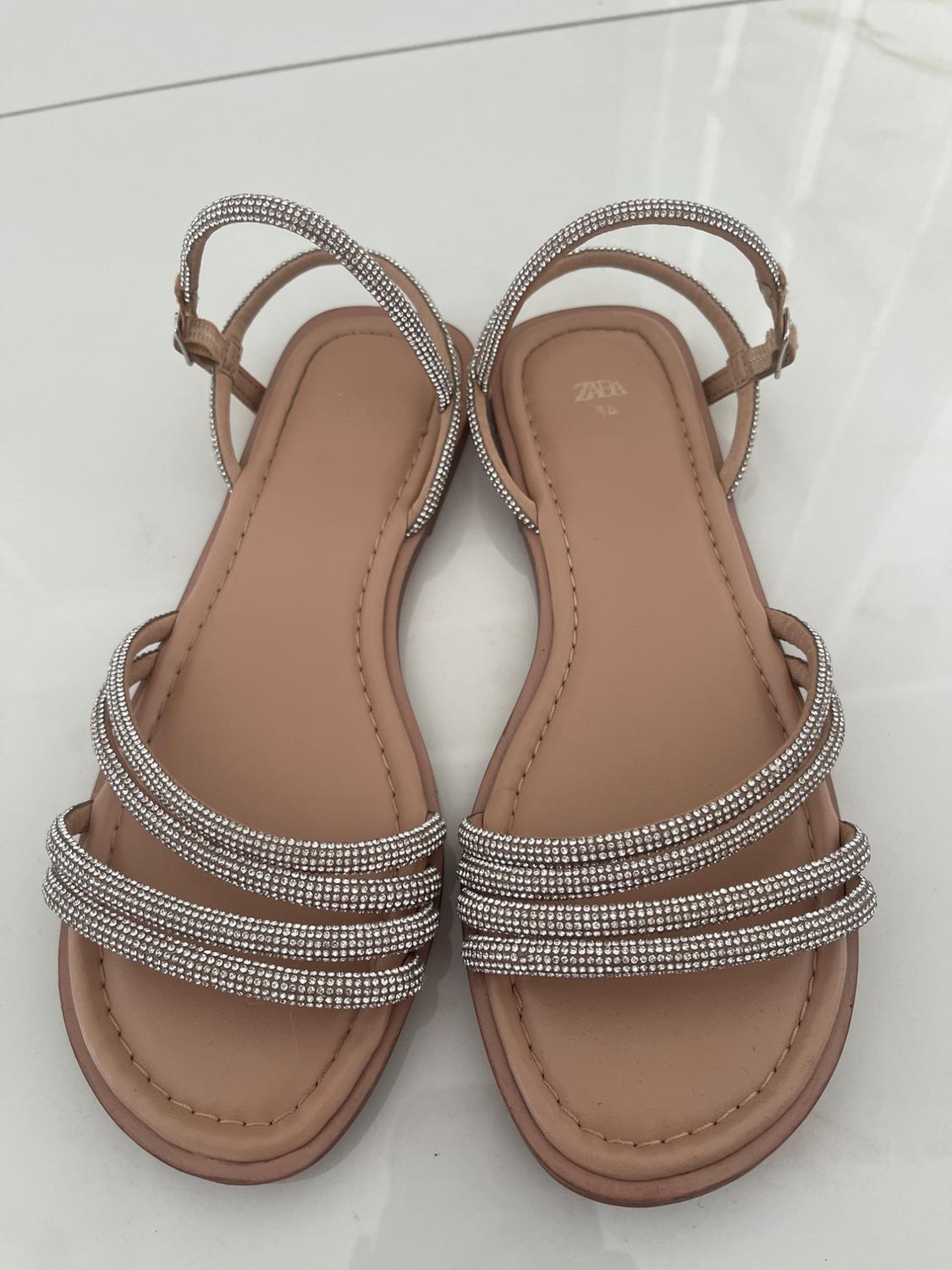 Beige flat sandals with rhinestone straps and ankle fastening on a light-coloured floor. Text: ZARA 36.