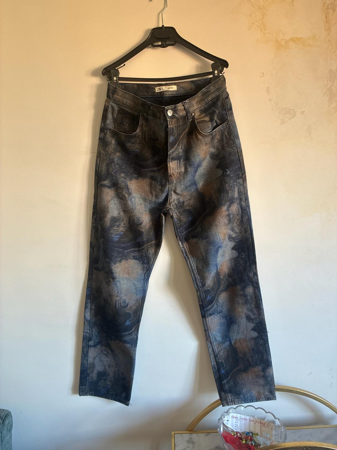 Τζιν παντελόνι ZARA με μαρμάρινο τύπωμα σε μπλε και καφέ αποχρώσεις, κρεμασμένο σε μια κρεμάστρα σε έναν ανοιχτόχρωμο τοίχο.