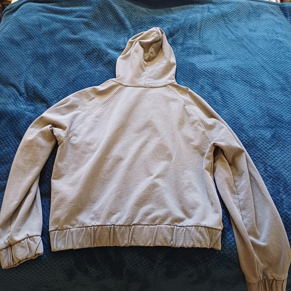 Beige hoodie seen from behind, placed on a textured blue bedspread.