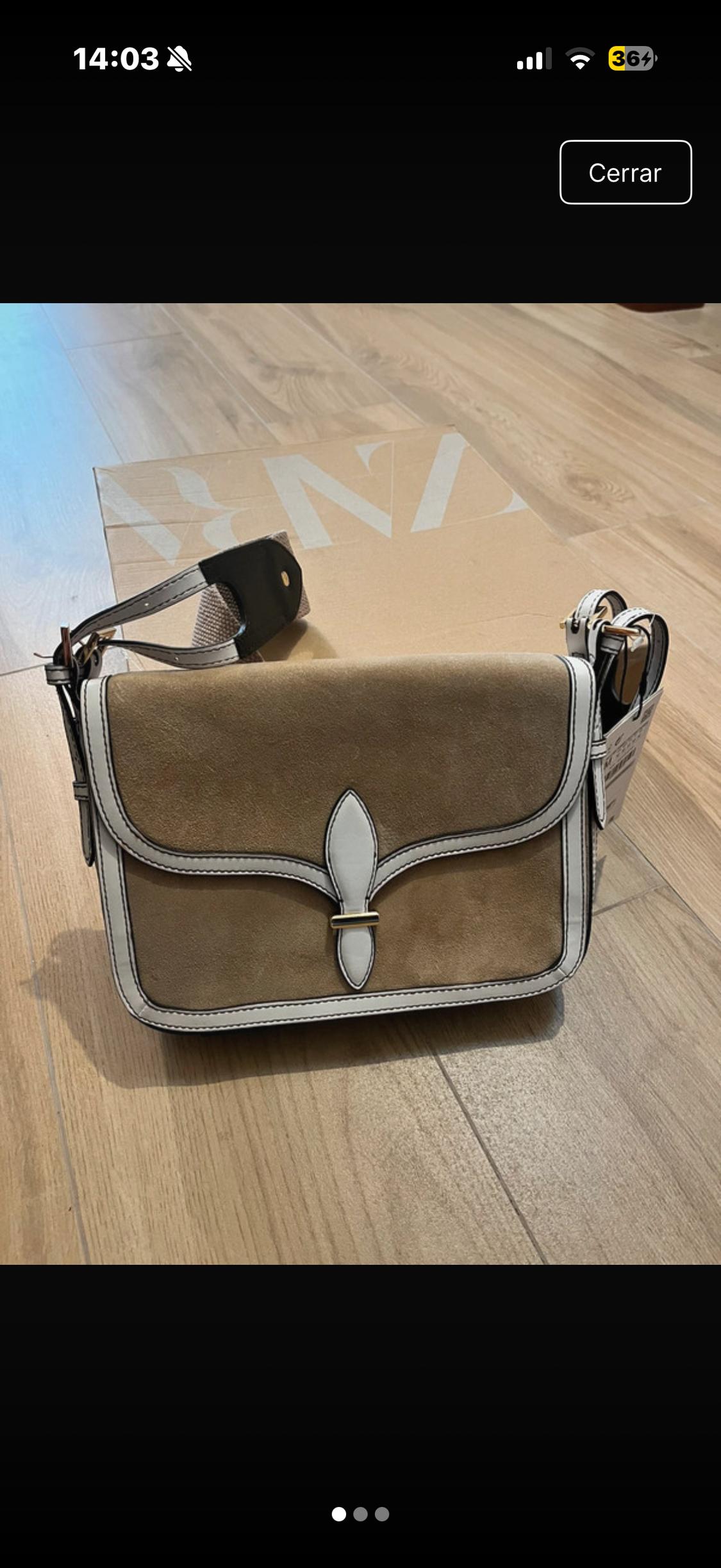 Brown leather bag with white details on a wooden floor. Cardboard box behind with visible white lettering.