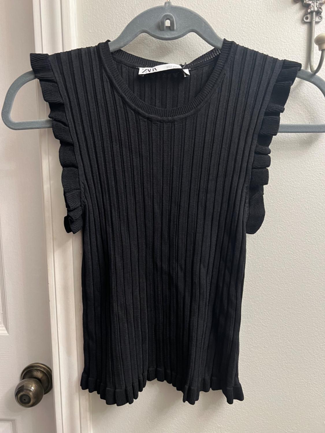 Front view of a black sleeveless blouse with ruffles and ribbed texture.