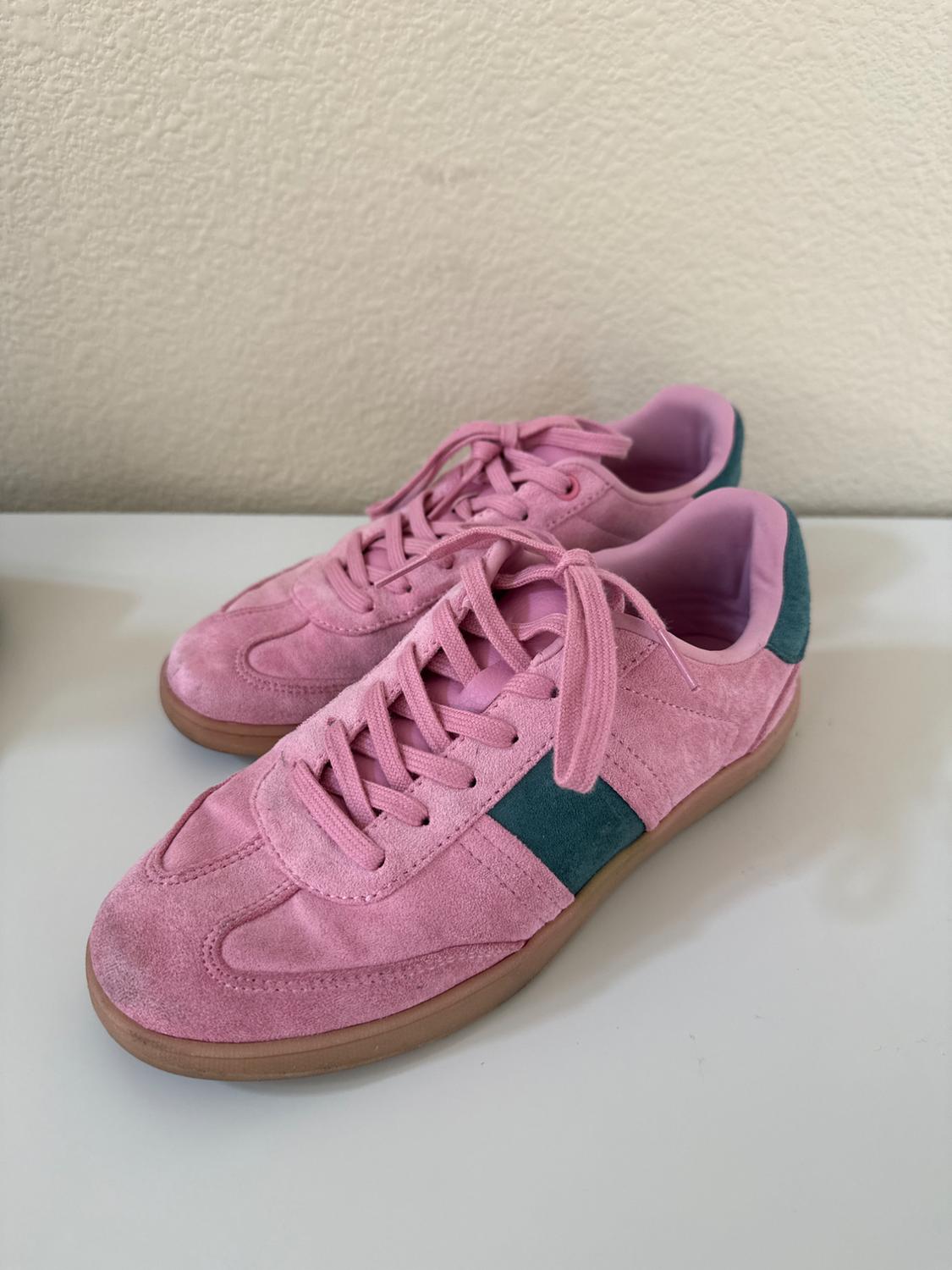 Pink suede sneakers with laces, rubber sole, and green detail on the side, on a white surface.