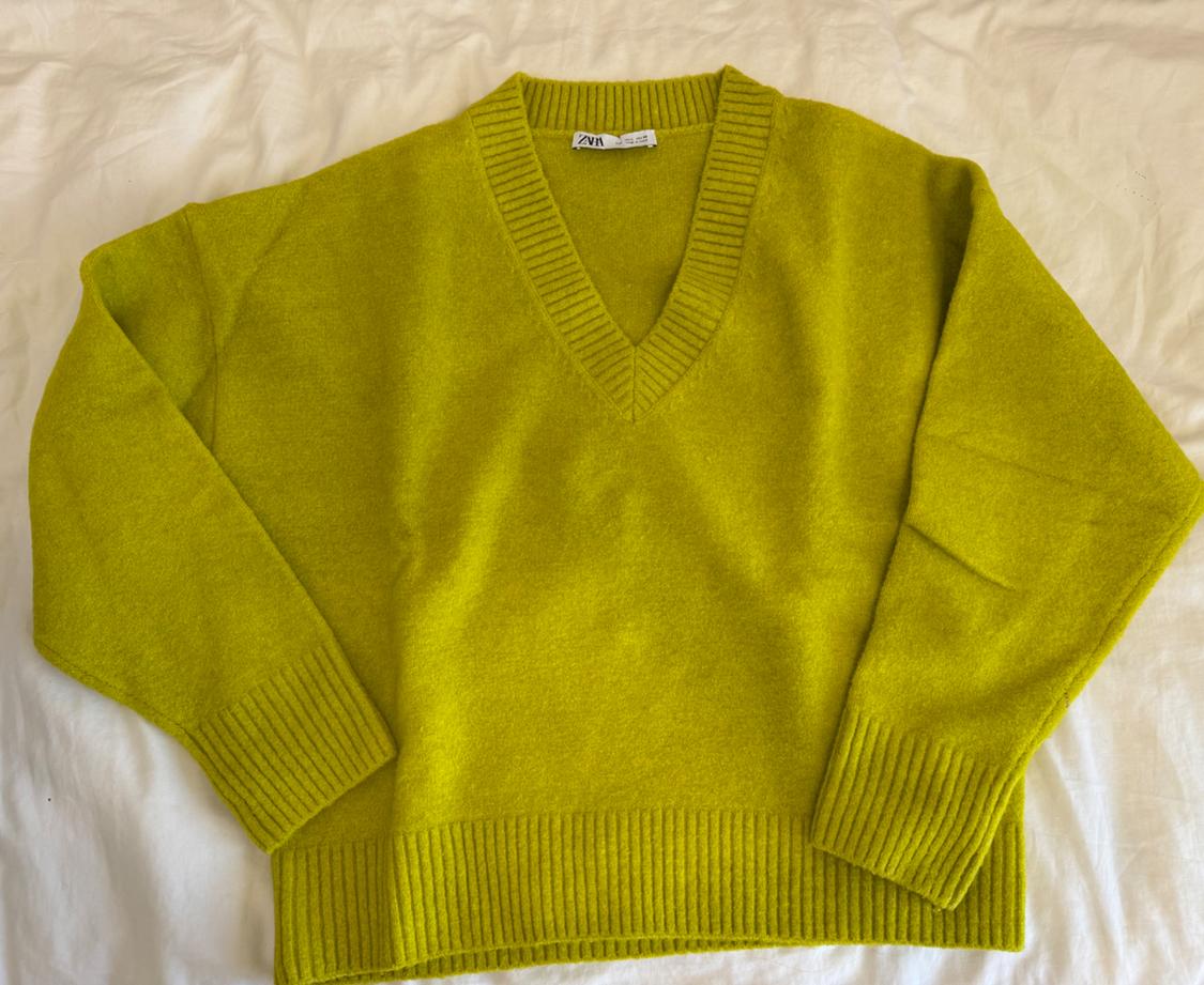 Lime green, long-sleeved, V-neck jumper with ribbed trims, on a crumpled white sheet. Label with the text ZARA.