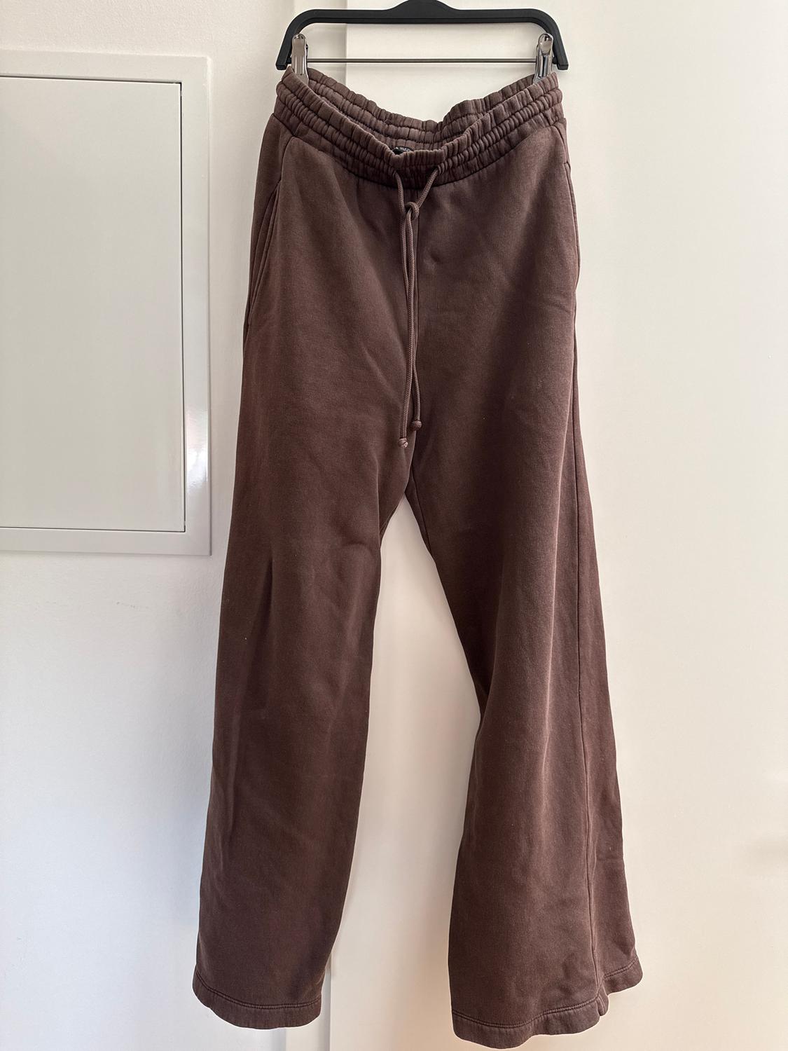 Brown jogging bottoms hanging on a black hanger against a white wall. Elasticated waist with adjustable drawstring.