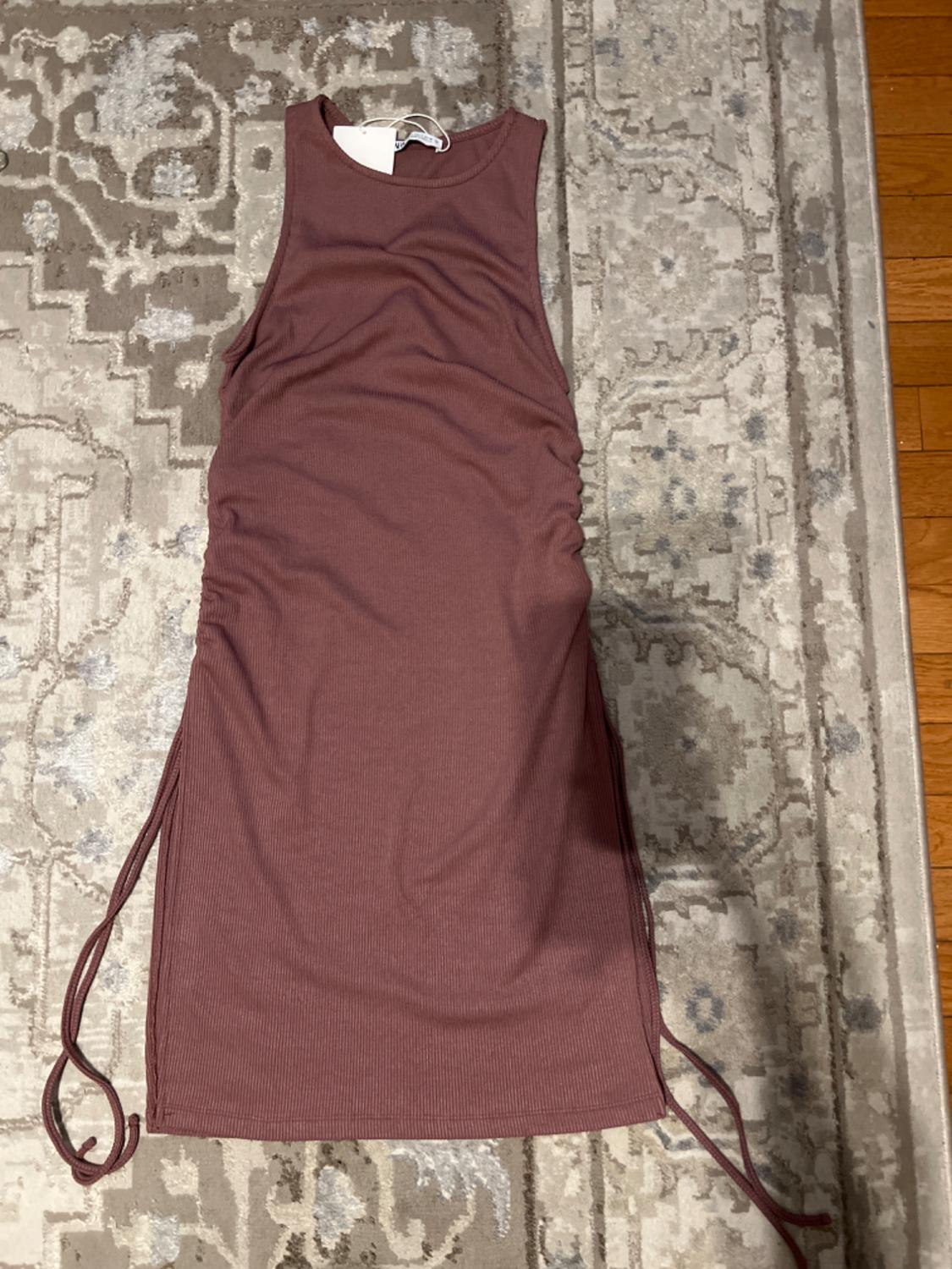 Sleeveless brown dress with side ruching and drawstrings, placed on a geometric design rug in beige and gray tones.