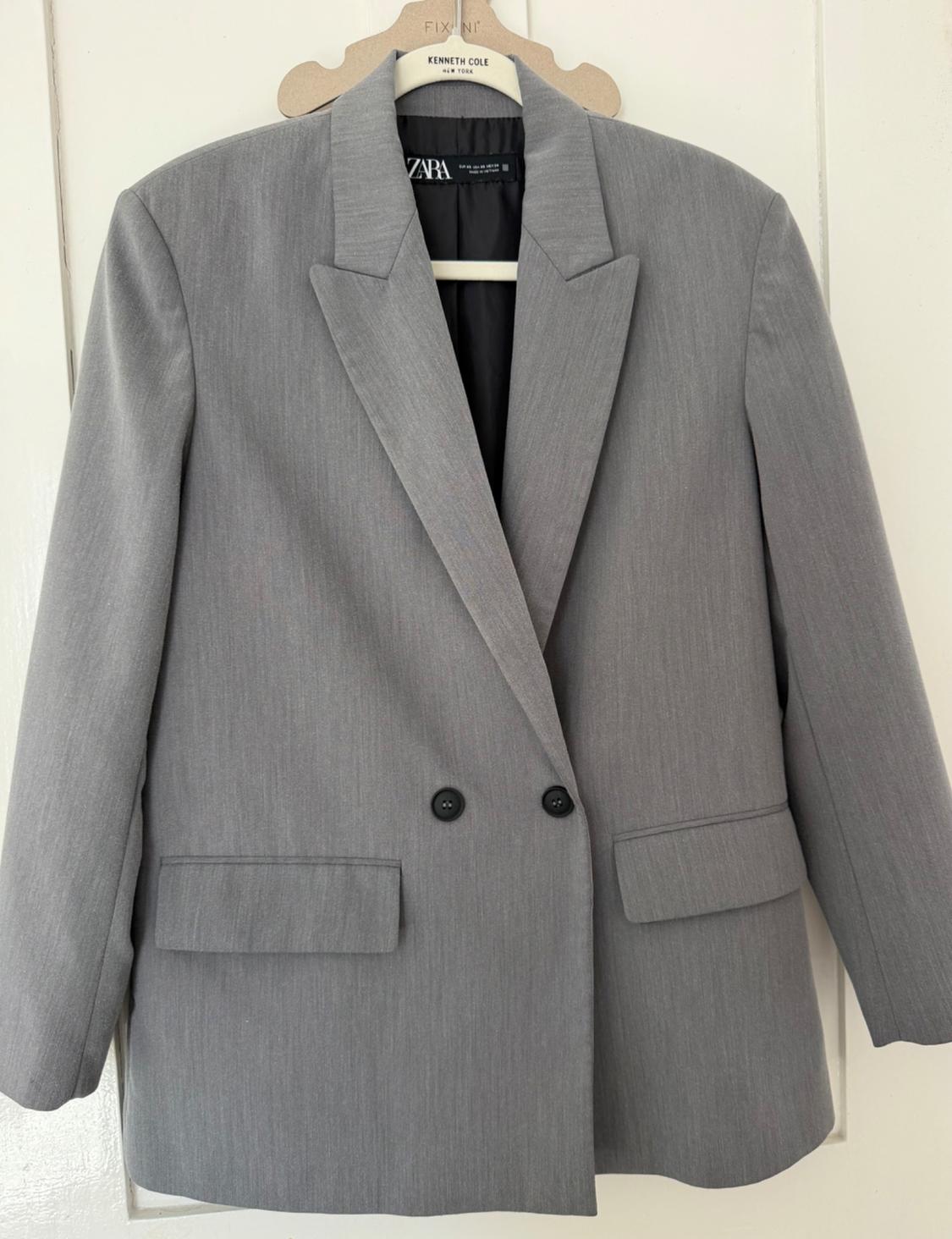 Grey double-breasted blazer with lapels and black buttons, hanging on a white door. Text: FIX NI, KENNETH COLE NEW YORK, ZARA.