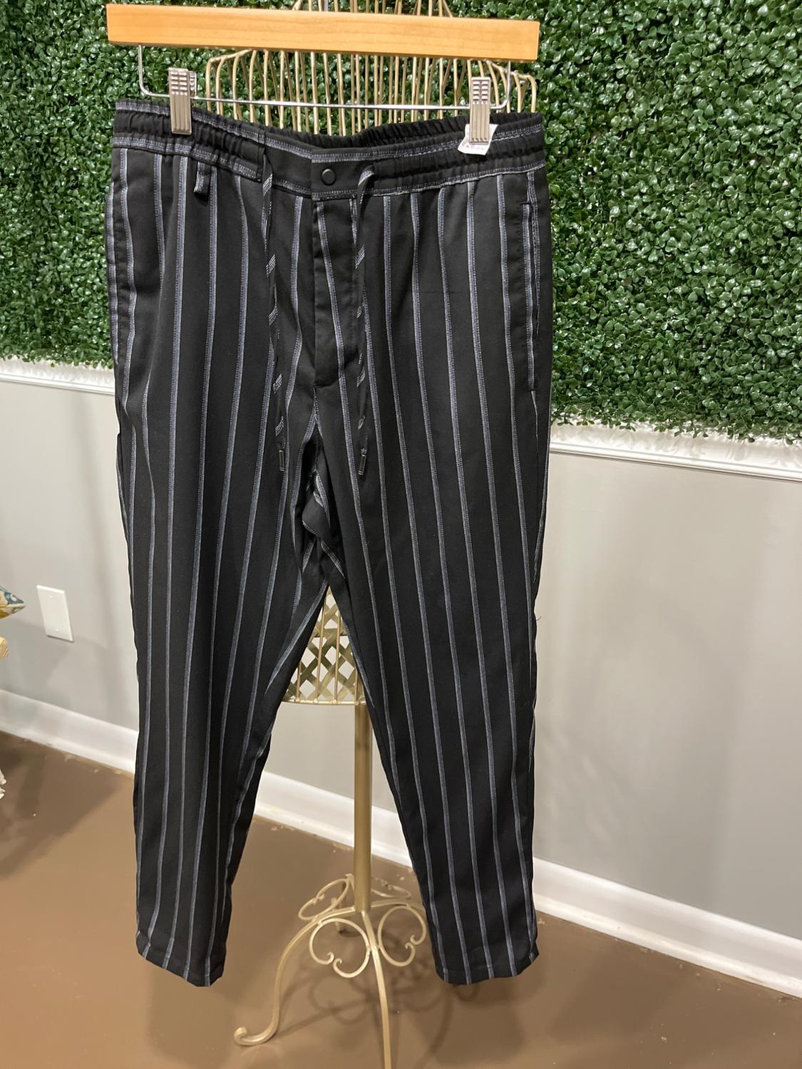 Black pants with gray vertical stripes hanging on a gold clothes rack, green wall background with leaf texture.