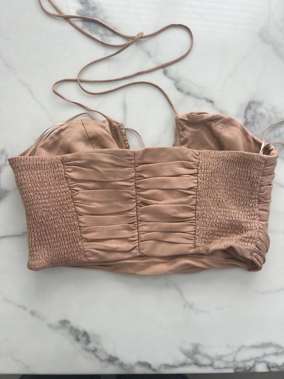 Beige spaghetti strap crop top with ruched sides, on a white marble surface.