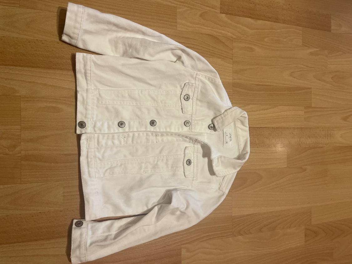 White denim jacket with metallic buttons on a light wooden floor. Long sleeves and classic collar.