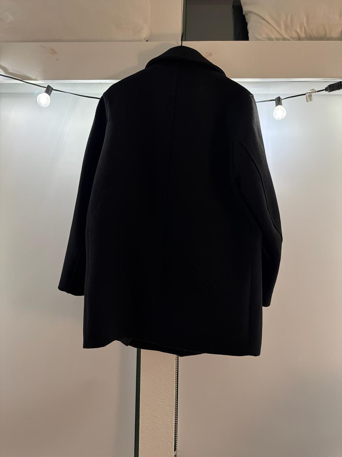 Black coat hanging backwards under a white shelf. In the background, a wall illuminated by a string of lights.