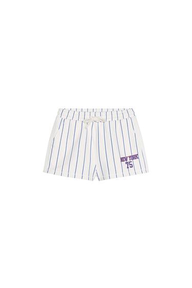 Front view of white shorts with blue stripes, text 'NEW YORK 75' on the right leg, side pockets.