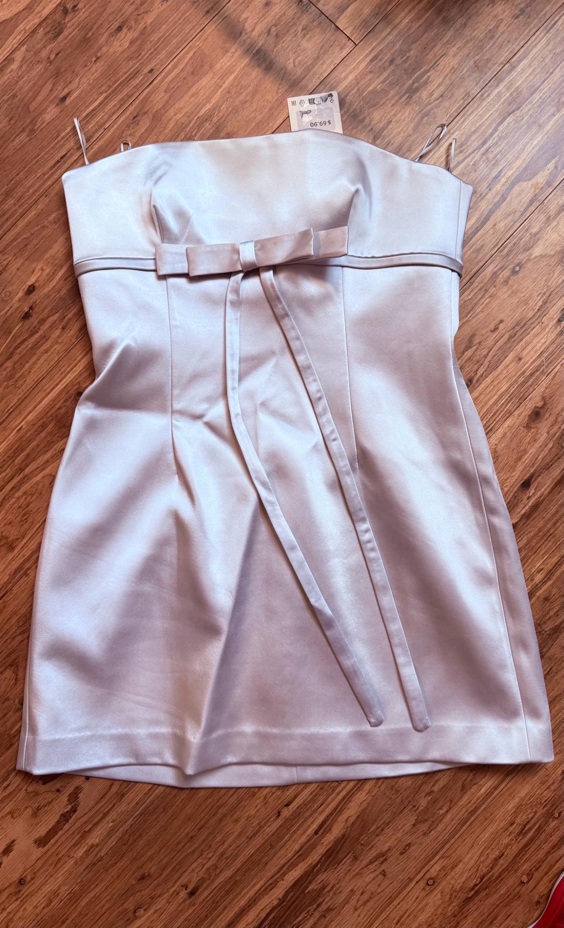 Light satin mini dress with a front bow and thin straps, laid out on a wooden floor. Tag with text $ 69.90.