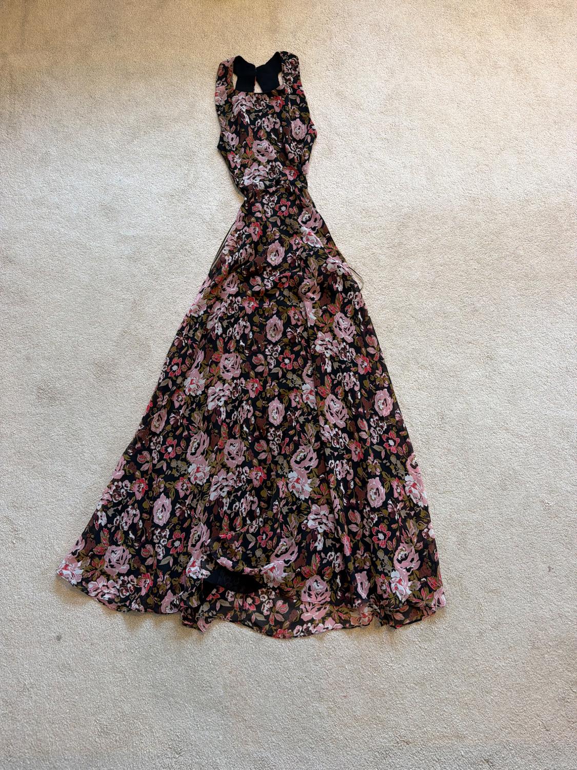 Long, flowing dress with a pink and brown floral print on a black background, laid out on a light beige carpet.