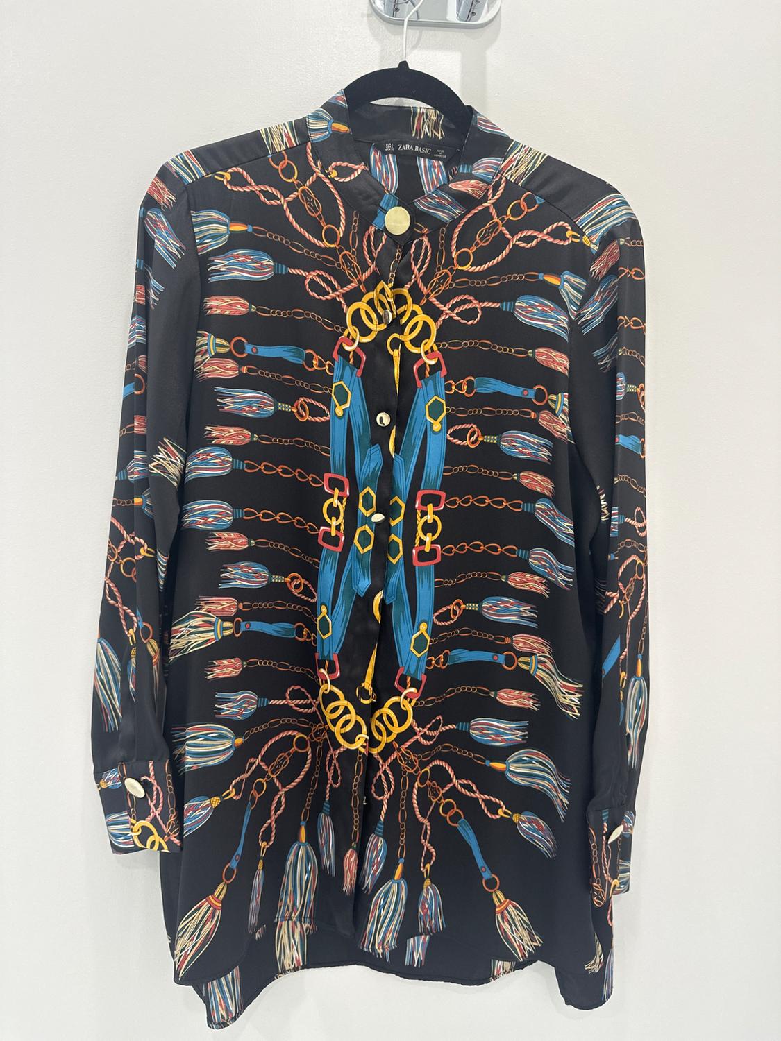 Long-sleeved shirt with a chain and tassel print in blue, red, and yellow on a black background, hanging on a hanger.