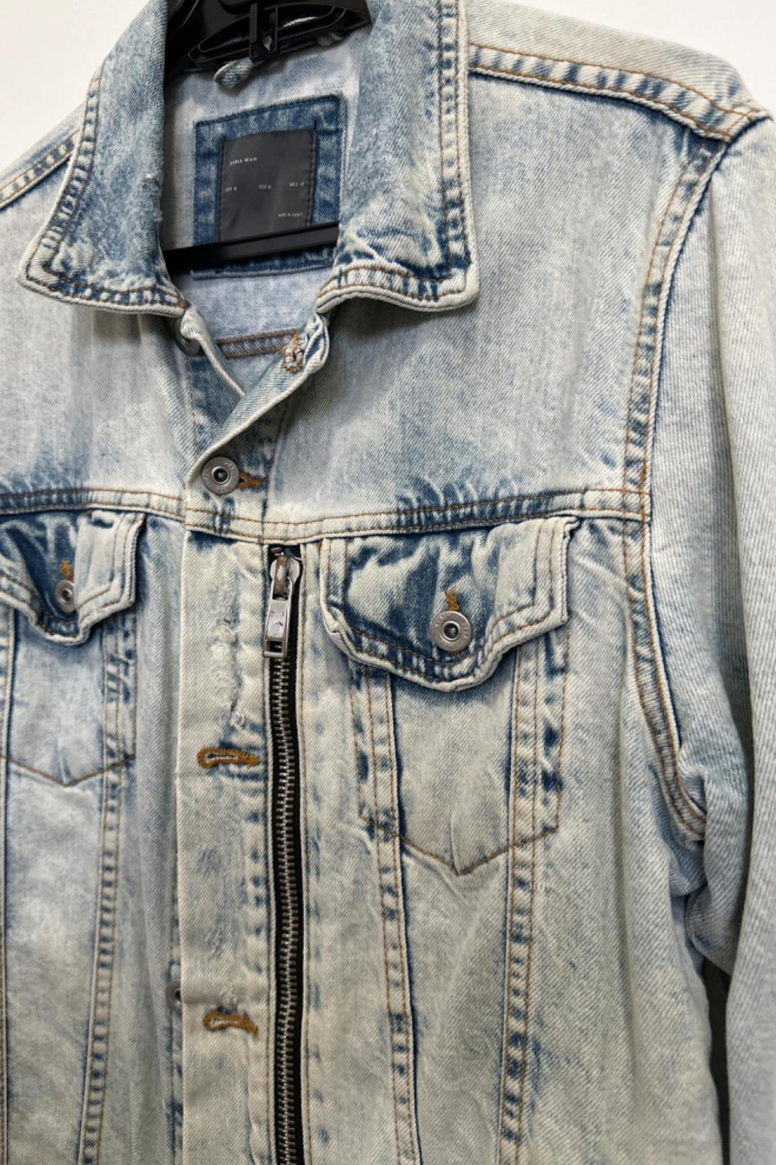 Detail of a light blue denim jacket with front pockets and a zip fastening.