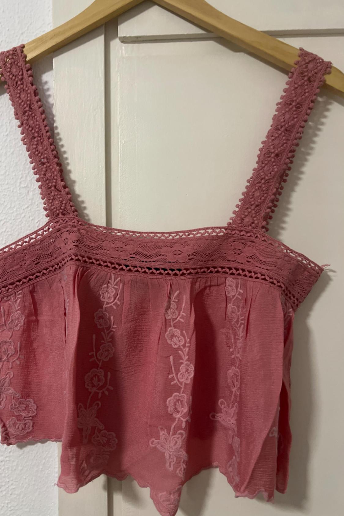 Detail of a pink top with lace straps and floral embroidery.