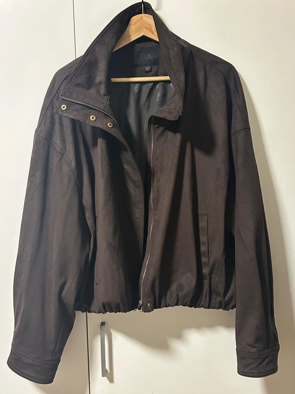 Brown jacket hanging on a wooden hanger, with a zip and buttons at the neck, against a white background.