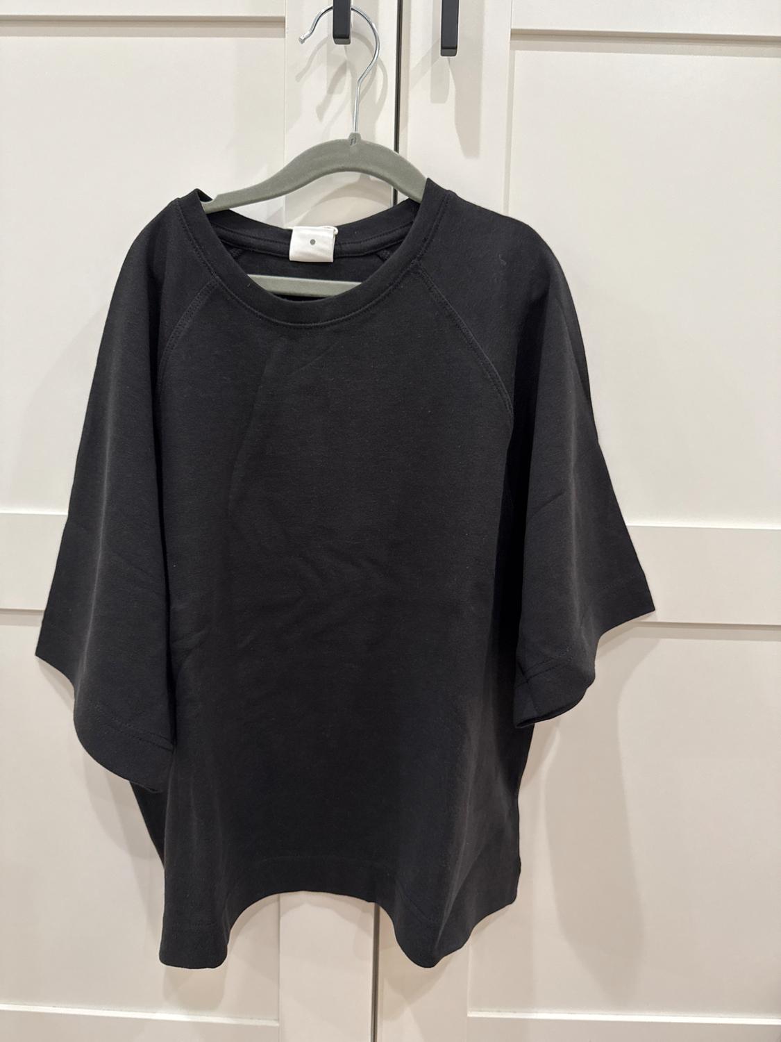 Black short-sleeved t-shirt hanging on a grey hanger over a white door.