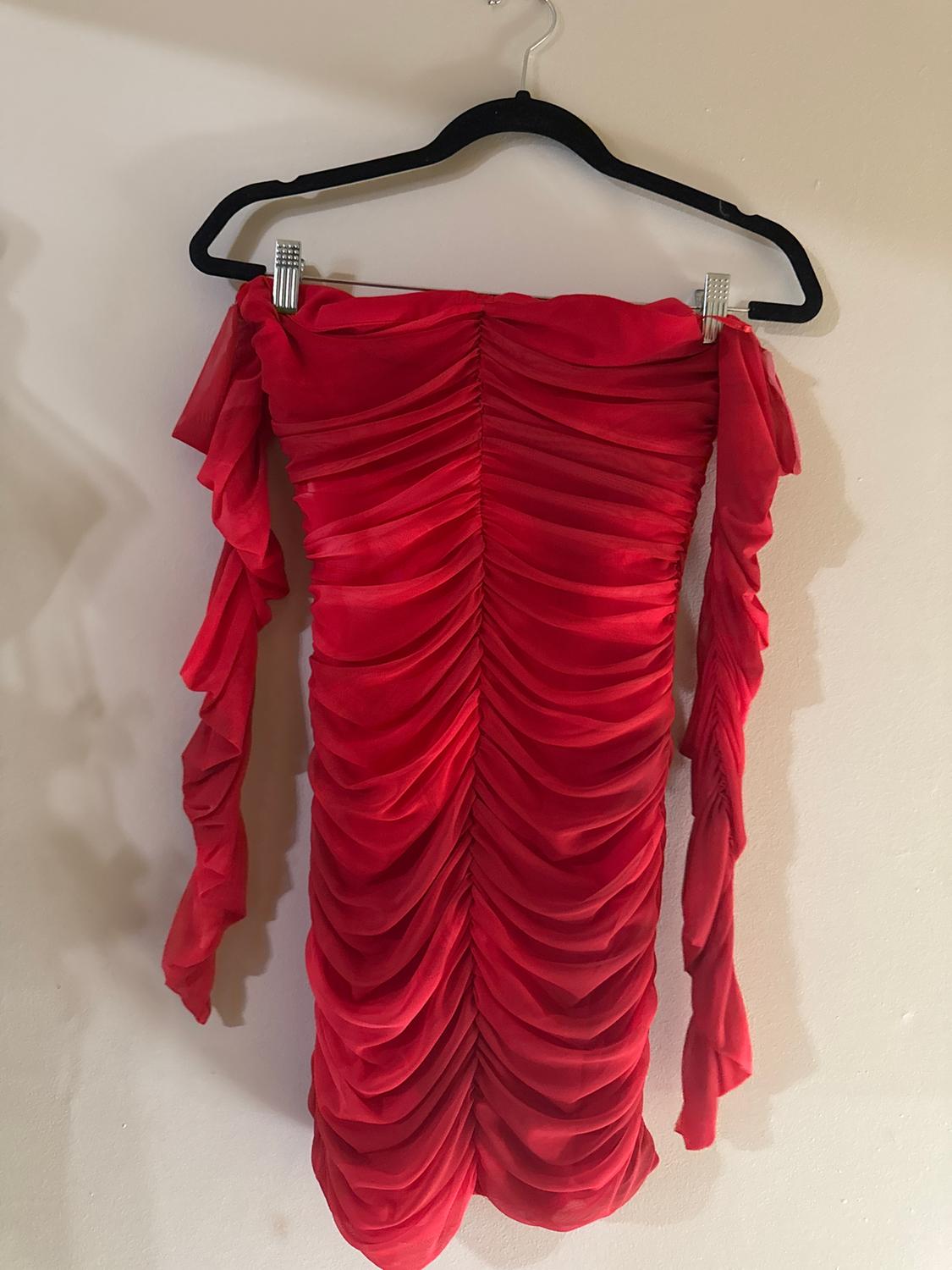 Ruched red dress with long sleeves hanging on a black hanger against a white wall.