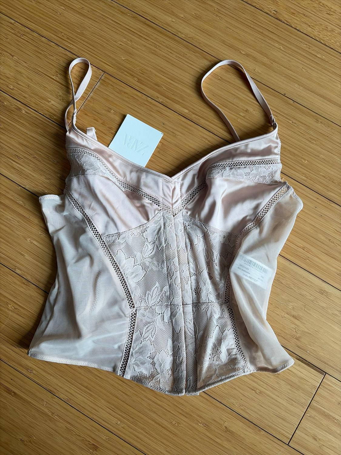 Light pink lingerie-style top with lace details and thin straps on a wooden floor. Tag with the text ZARA.