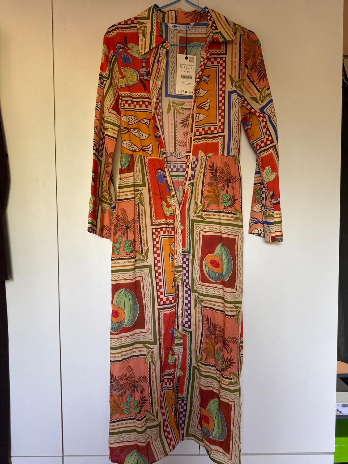 Long dress with a colourful fruit and leaf print, hanging on a blue hanger. Label visible at the neck.