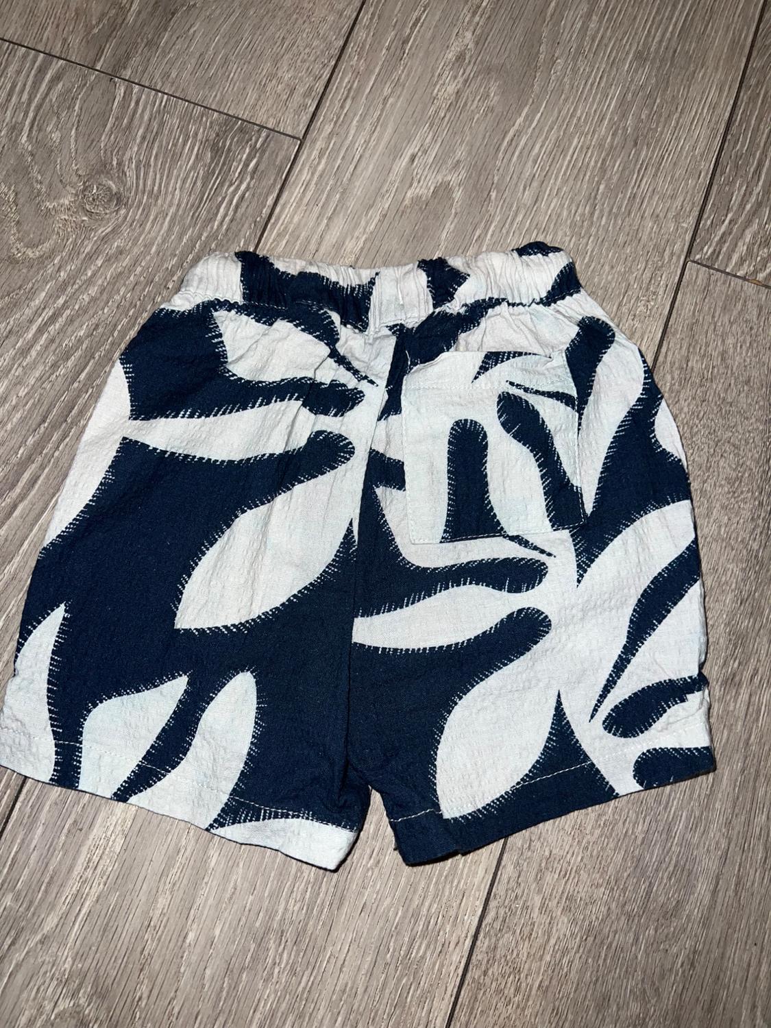 Shorts with a white leaf print on a dark blue background, placed on a light wood floor.