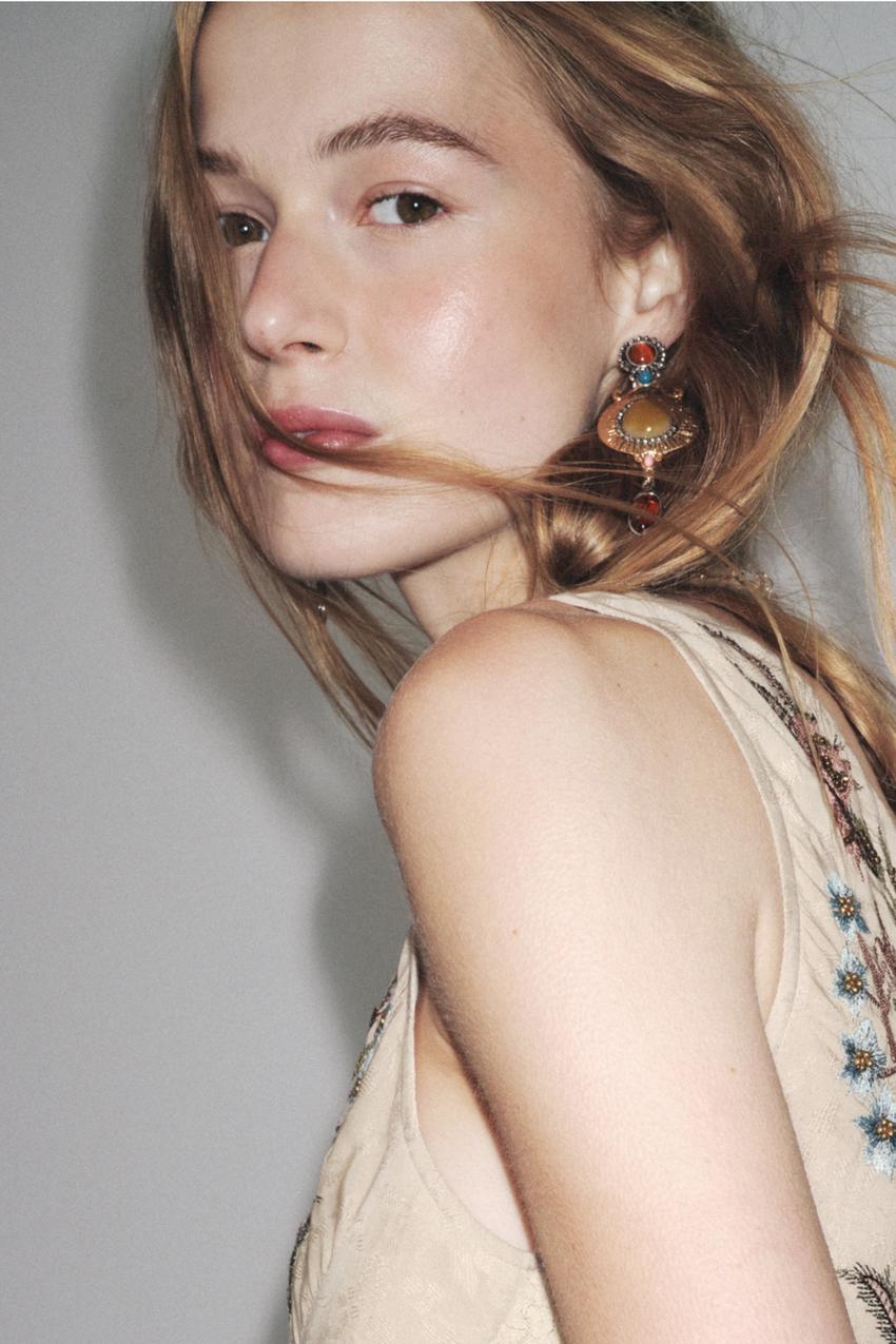 Details of dangling earrings in gold and silver with colored stones. Closure with nut and clip.