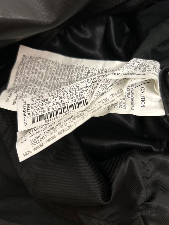 Clothing label with multi-language text, including care instructions and material composition, on black fabric.