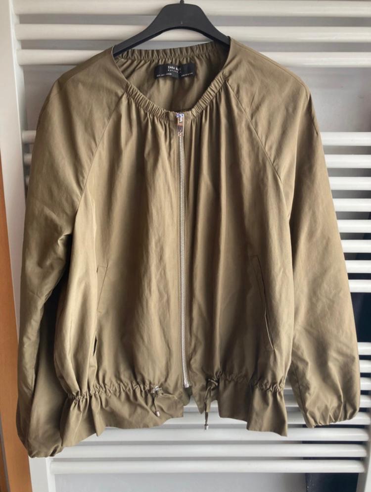 Khaki jacket with zip and elasticated waist and cuffs, hanging on a black hanger in front of a white background.