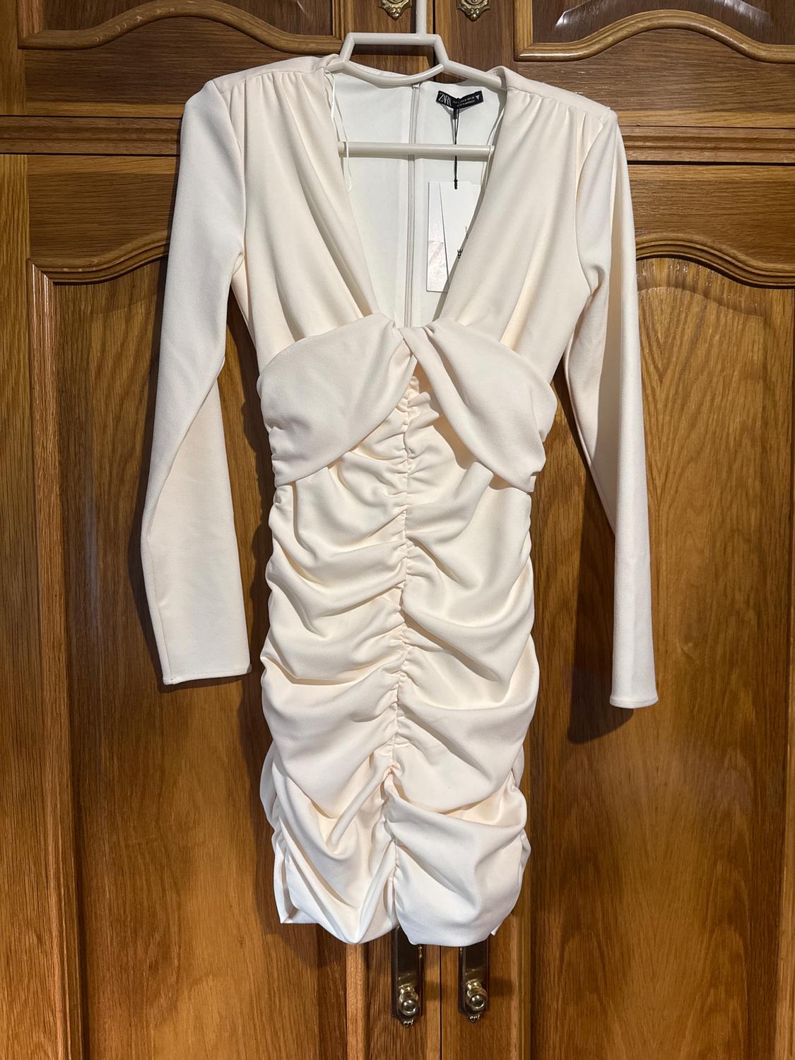 Beige dress with long sleeves and ruching on the front, hanging on a hanger in front of a wooden door.