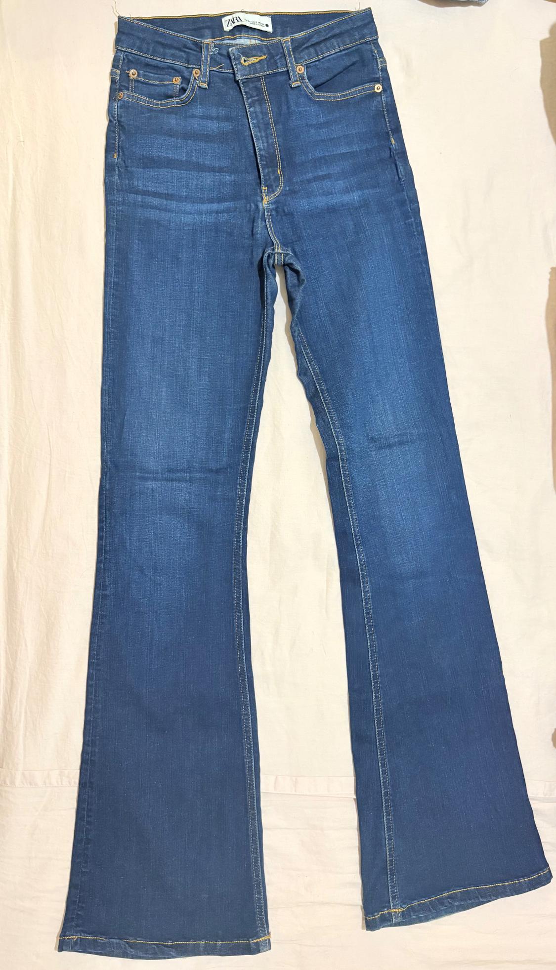 Blue flared jeans with yellow stitching on a light-wash denim background. ZARA label visible on the waistband.