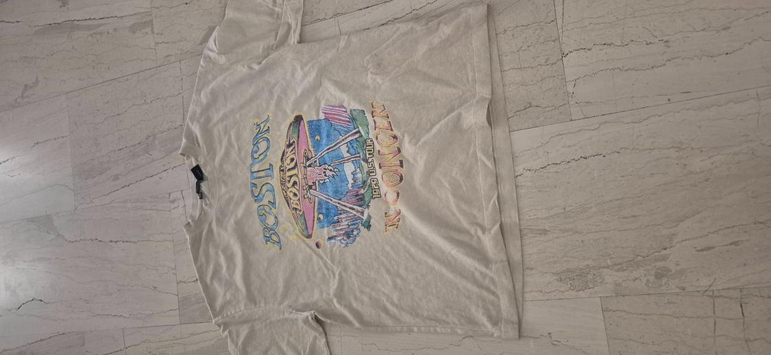 White t-shirt with colourful rocket design and "BOSTON" text on the front, on a light marble floor.
