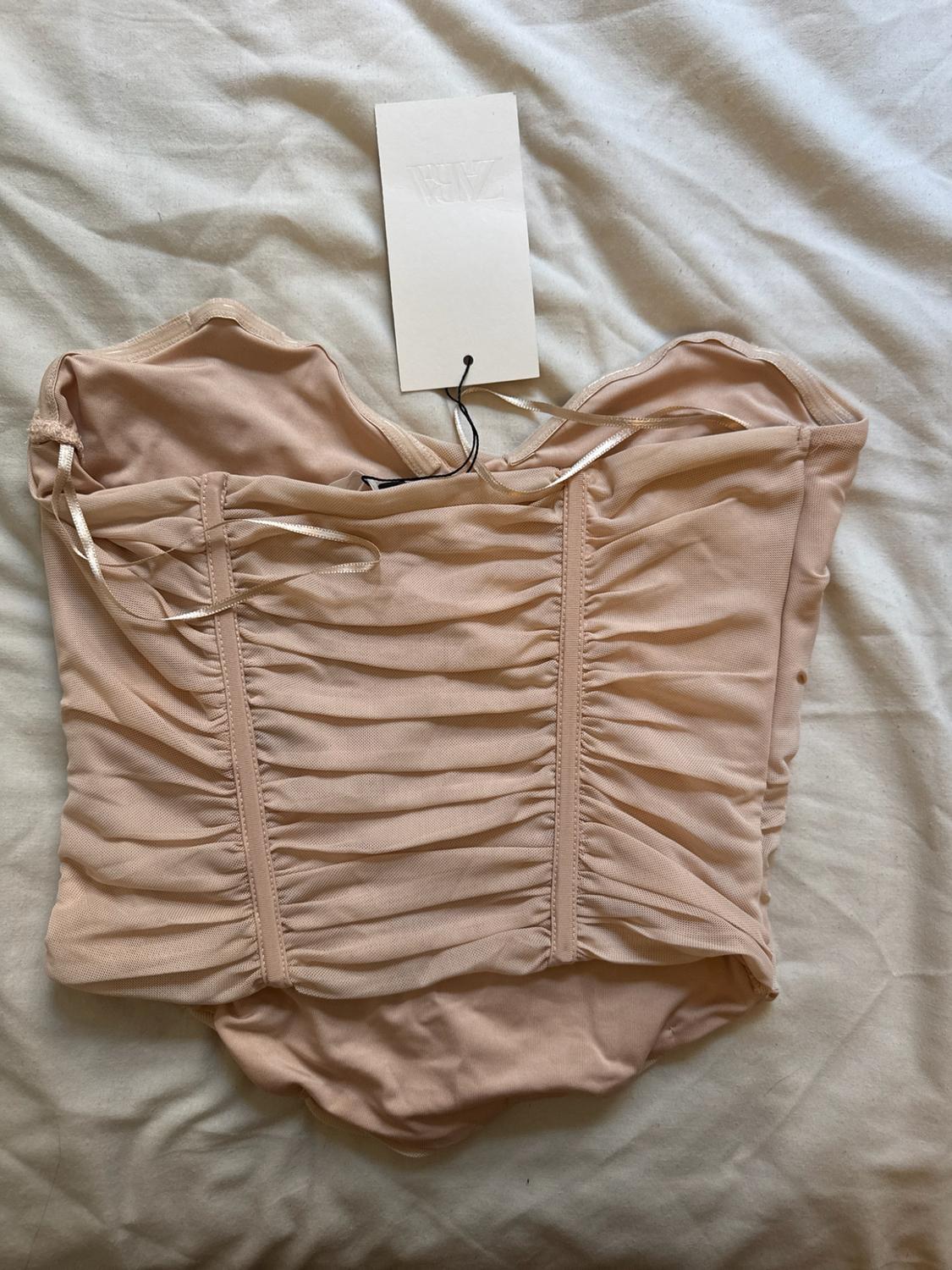 Nude tulle gathered top on a crumpled white sheet. Label with the text ZARA.