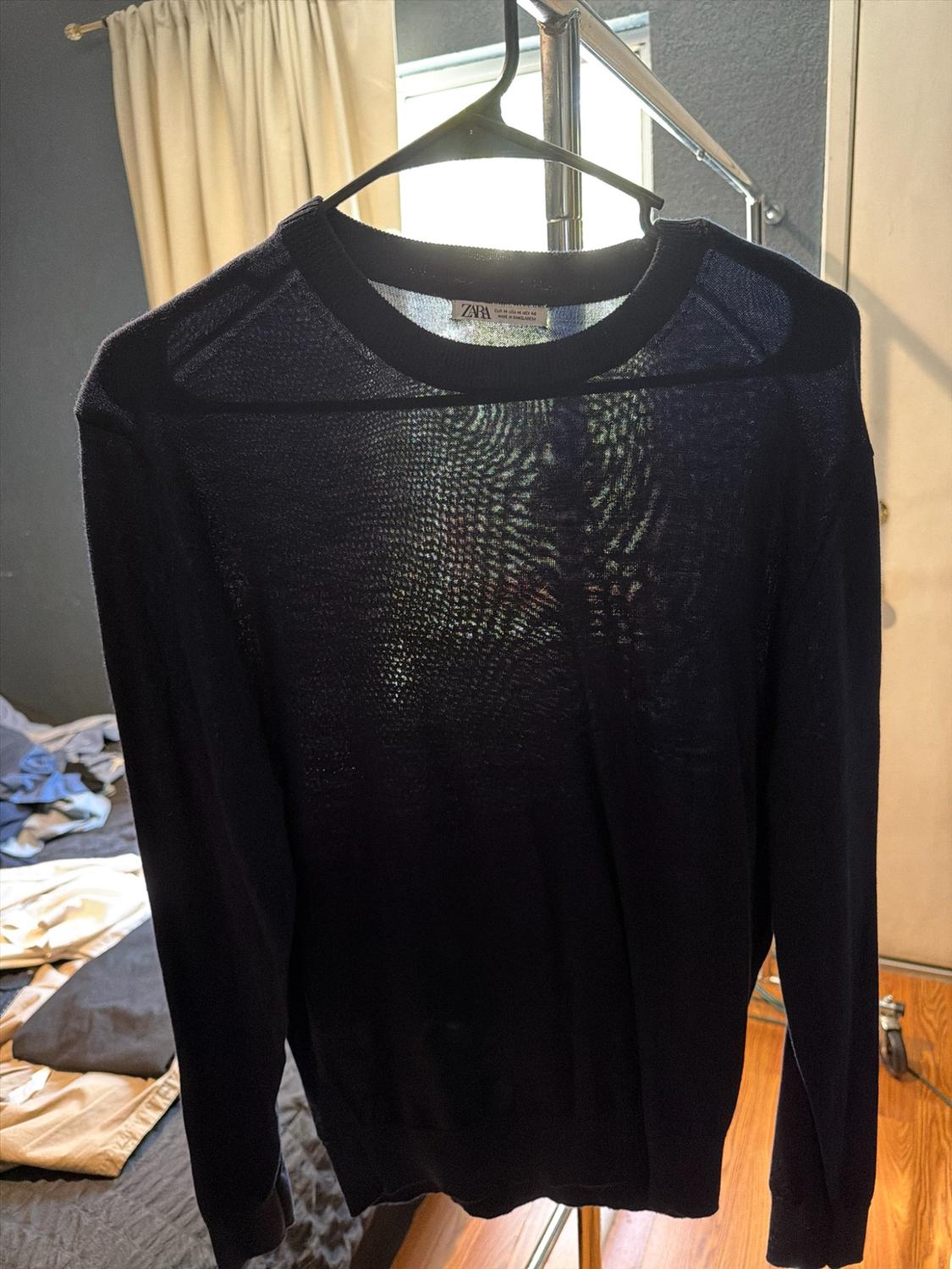 Dark semi-sheer long-sleeved sweater on a hanger. Tag reads ZARA EUR M USA M MEX 40. Room background.