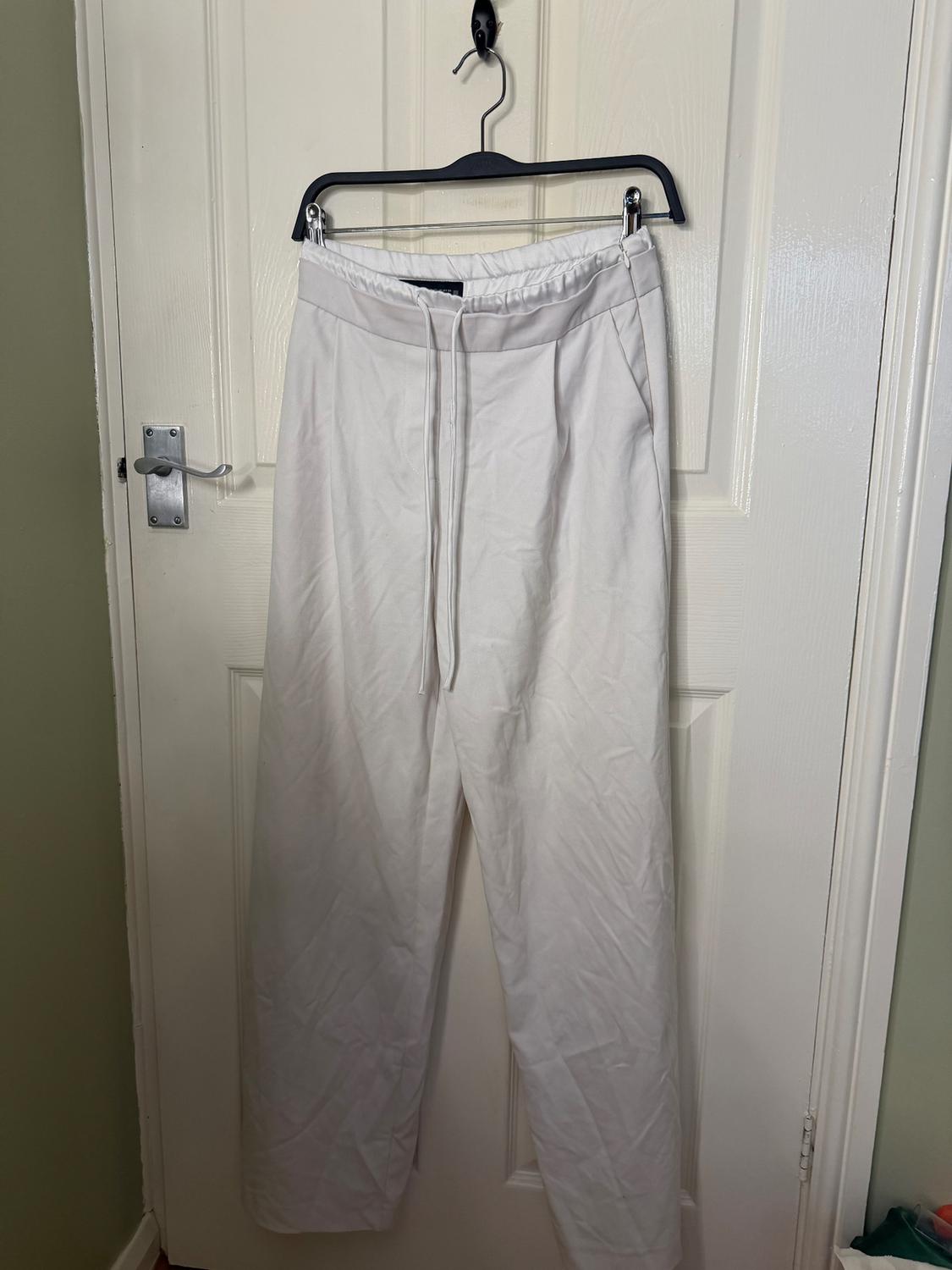 White trousers hanging on a black hanger over a white door. The door has a silver handle.