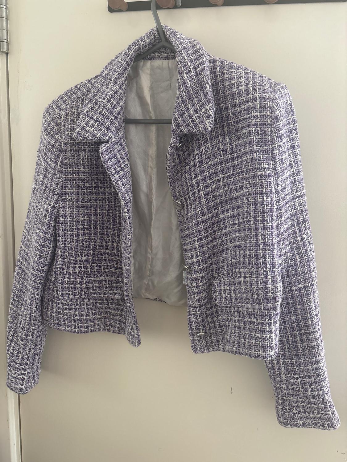 A purple and white jacket is hanging on a coat hanger over a white door. It features a classic design with lapels and pockets.