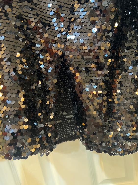 Shimmering fabric with silver and gold sequins, creating a dazzling effect. Blurred white background.