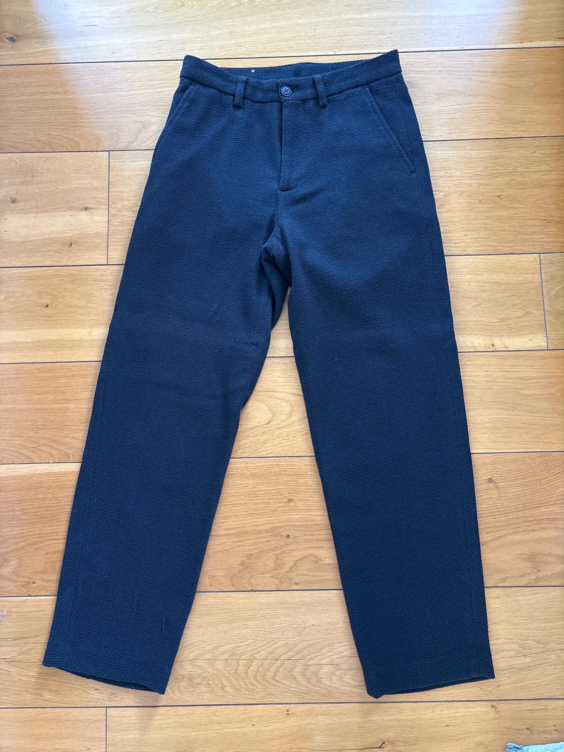 Front view of black trousers with side pockets and a front button.