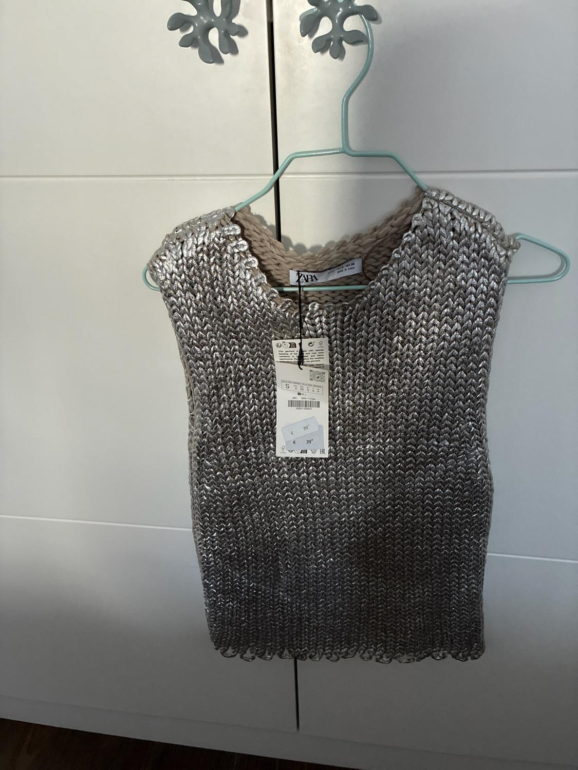 Silver sleeveless knitted top hanging on a blue hanger in a white wardrobe. Labels with the text ZARA, S and 39.
