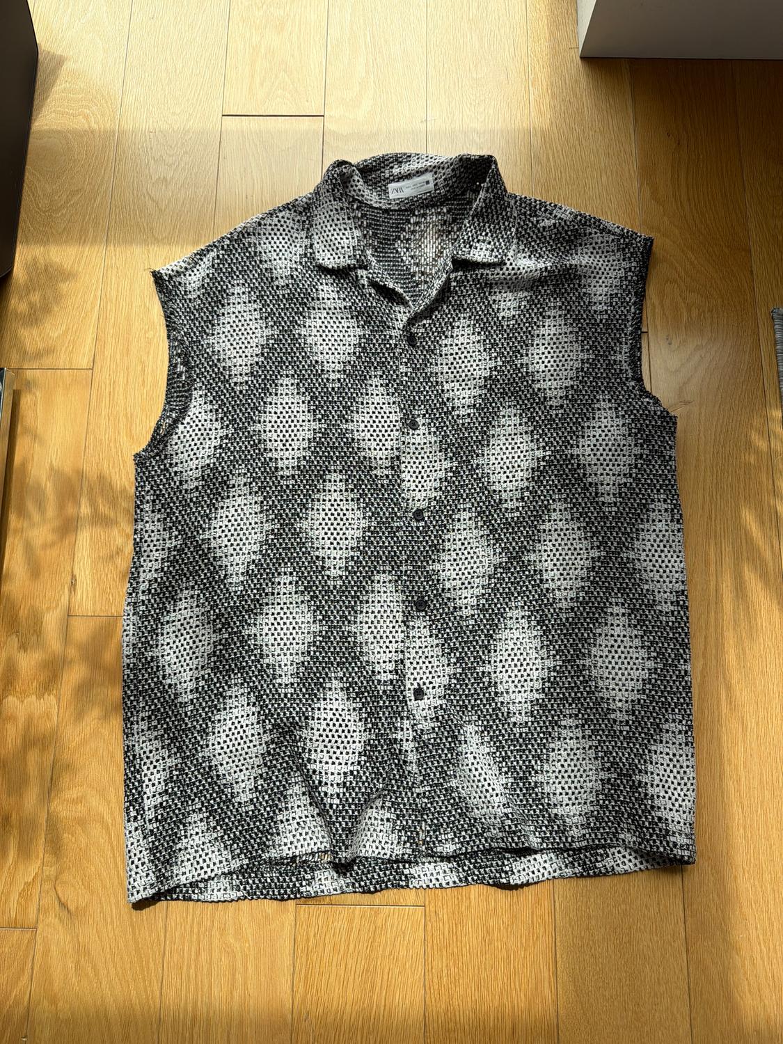 Sleeveless shirt with black and white geometric print on light wood floor. Natural light illuminates the scene.