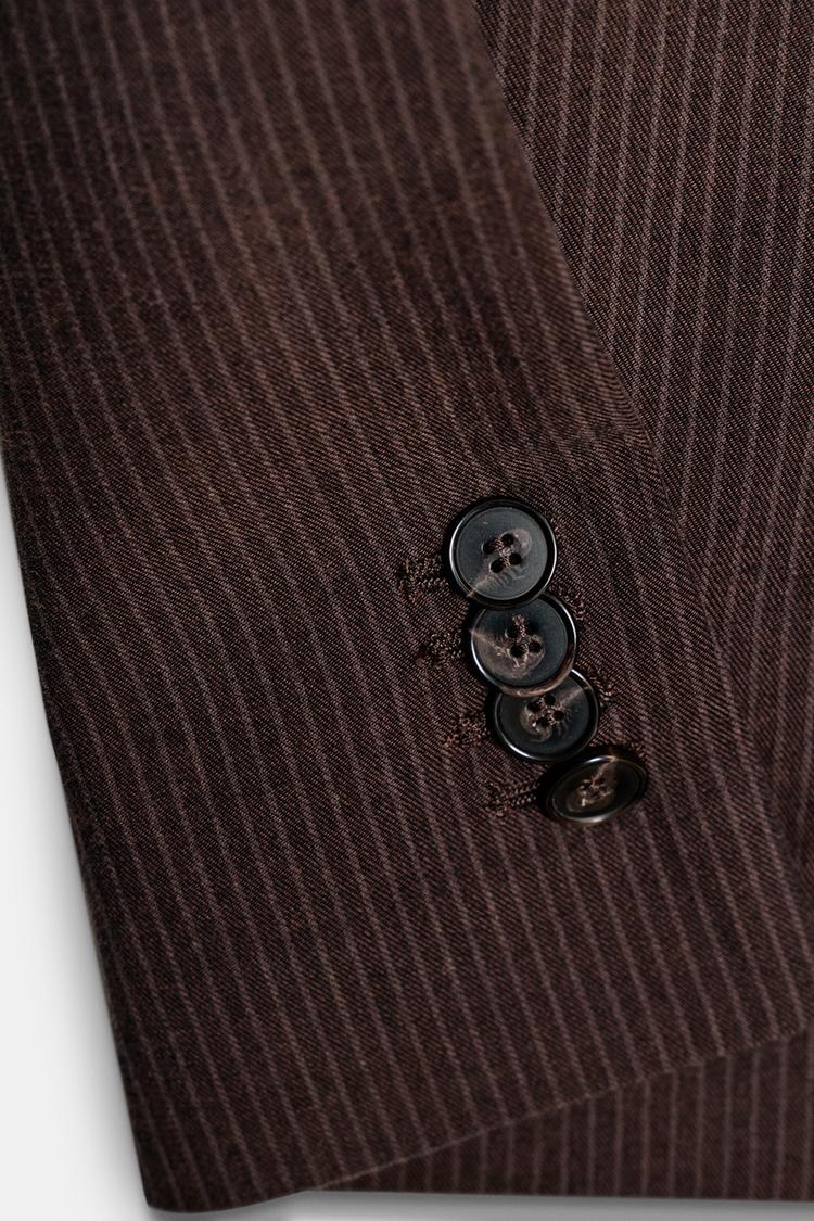 Detail of a brown marl jacket sleeve with stripes and four dark buttons.