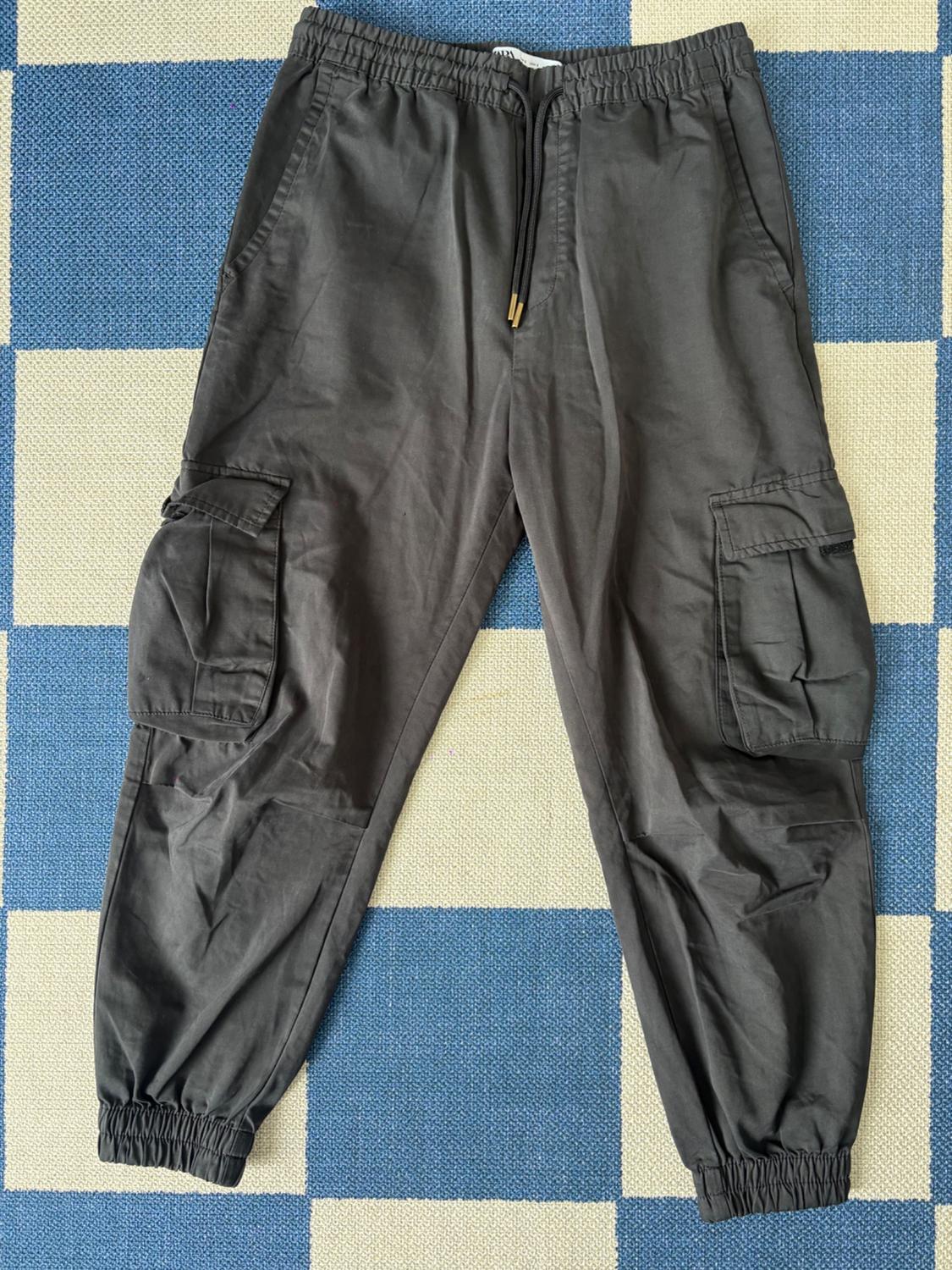 Gray cargo pants with side pockets and elastic waistband, on a blue and beige checkered rug.
