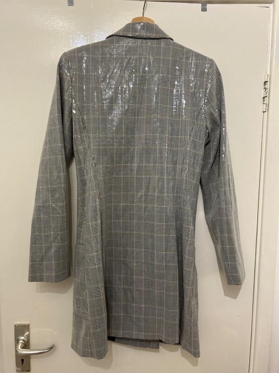 Long grey checked coat hanging on a white door. Fabric with a shiny finish and classic lapels.