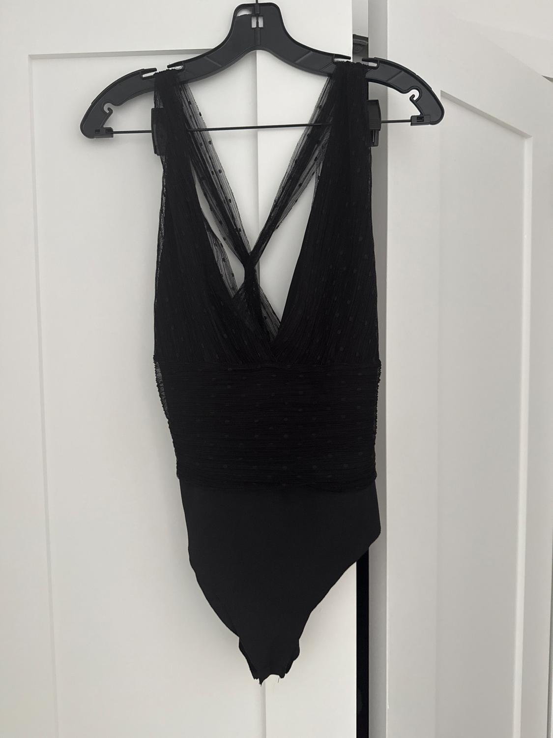 Black bodysuit with criss-cross tulle straps on the back, hanging on a black hanger over a white door.