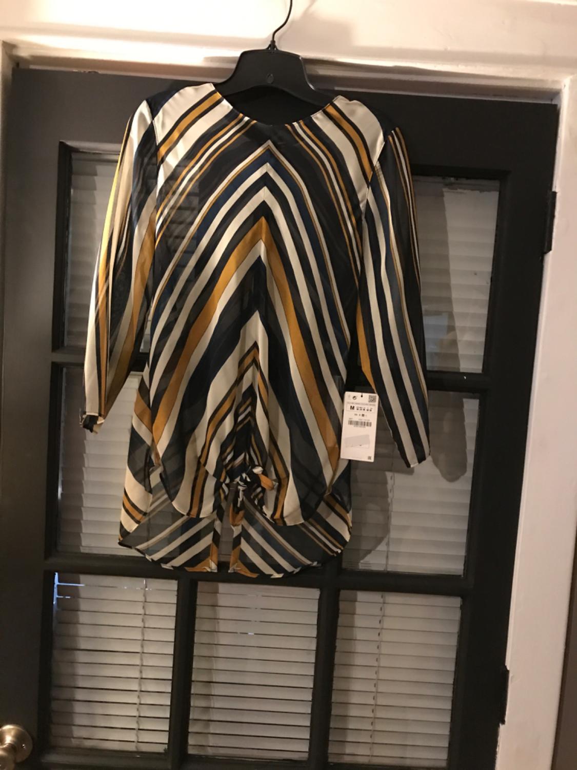 Front view of a blouse with a black, white, and gold stripe print, featuring a tie at the hem.
