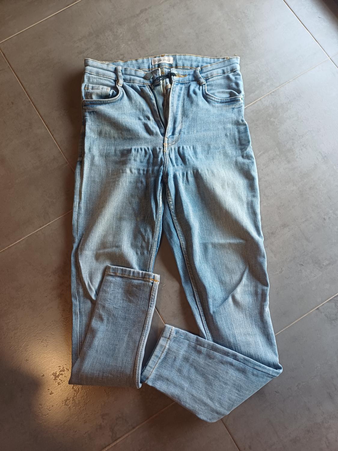 Light blue jeans, slightly wrinkled and with the button undone, on a grey tiled floor.