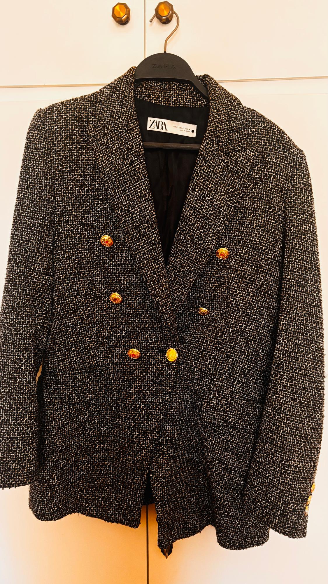 Textured blazer on a black Zara hanger, with gold buttons, hanging against a light background.