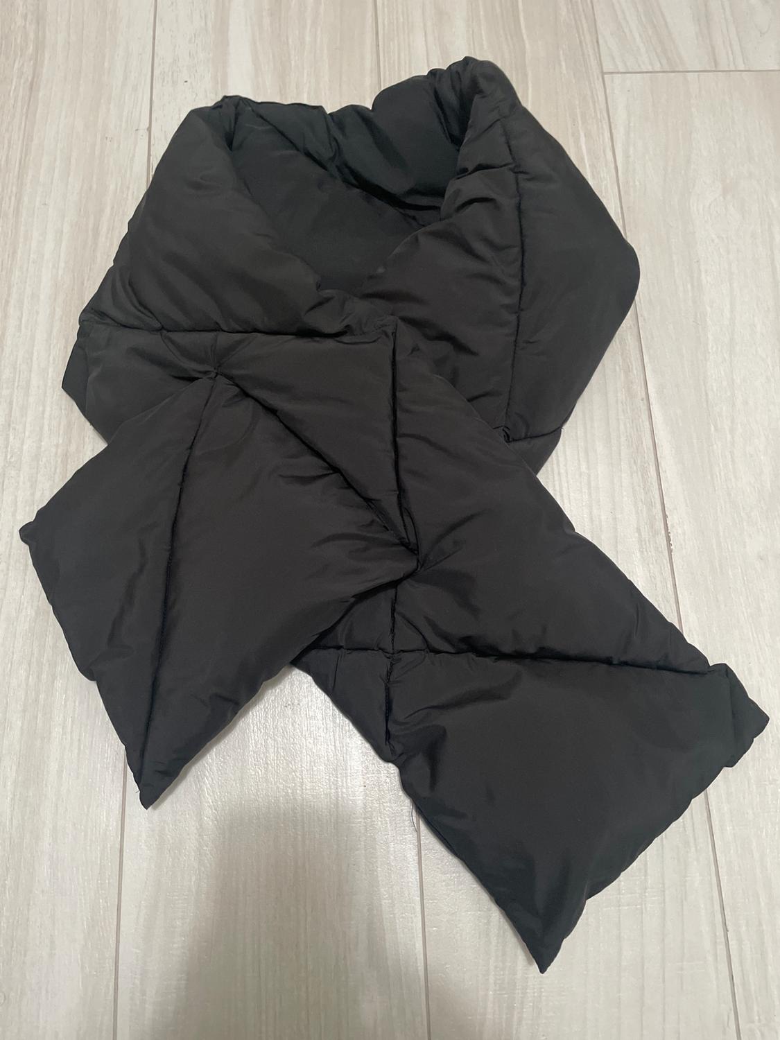 Black quilted scarf on a light wood floor, with a crossover design and soft texture.