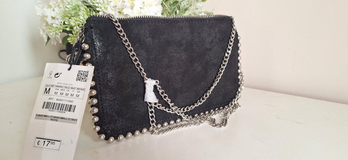 Black bag with studs and silver chain. White flowers in the background. Text: www.zara.com M ART.: 6045/111/040 £17.95.