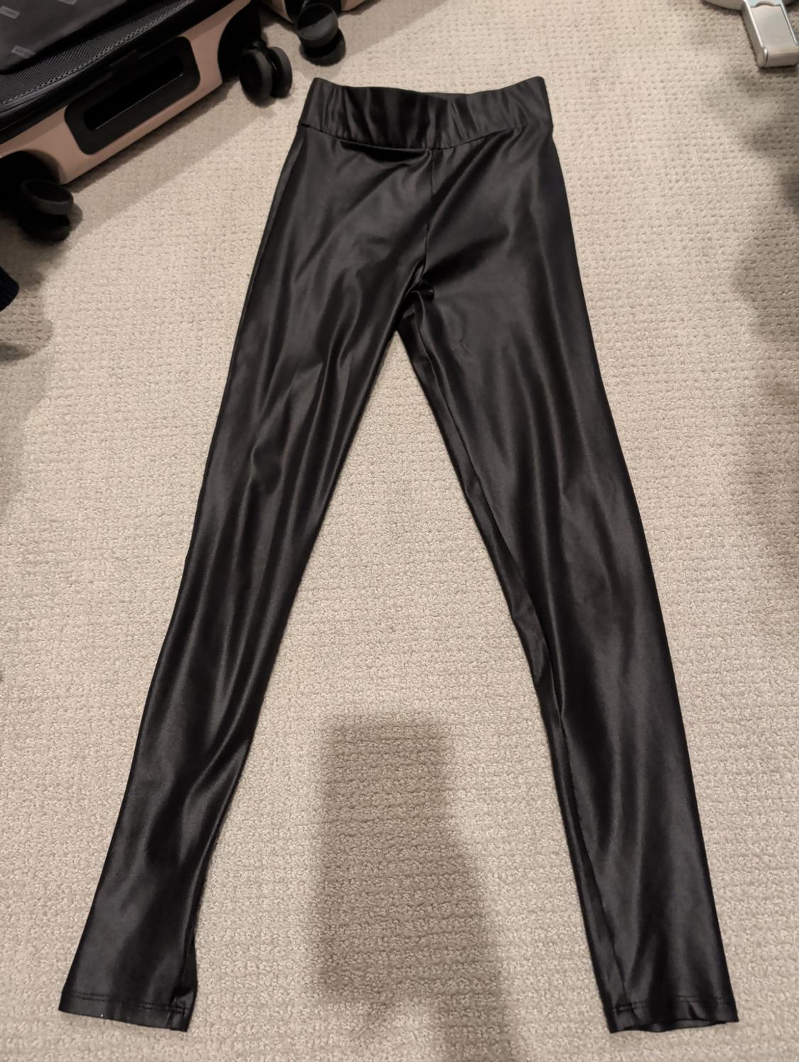 Black shiny fabric leggings on a beige carpet, next to a black wheeled suitcase.